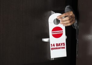 Hand holding do not disturb tag on the door knob. 14 day quarantine for Coronavirus.